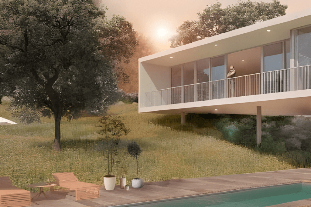 Vista de una casa moderna sobre un paisaje verde, con piscina, árboles y una persona en el balcón al atardecer.