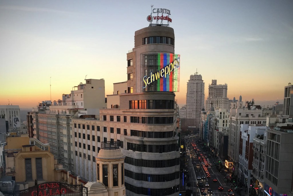 Vista de la Gran Vía en Madrid al atardecer, con el famoso edificio de Schweppes y neón en el centro.